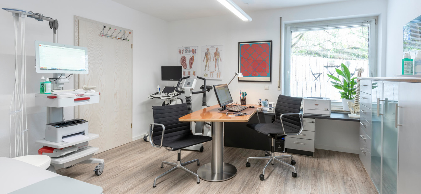 Helles Sprechzimmer mit Schreibtisch, Behandlungsstuhl und medizinischer Ausstattung.